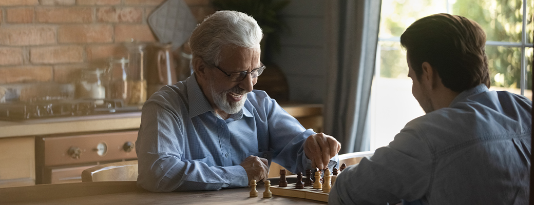 Image of senior male and middle aged male playing chess at kitchen table